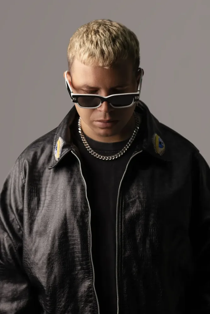 Tom Enzy in a black leather jacket and white-framed sunglasses, head lowered